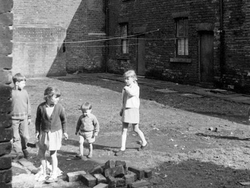 Terraced houses on Back Barker Square. Children are playing on the unmade road and a pile of bricks and rubble are in the foreground.