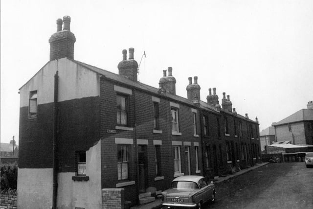 Brick through terraced houses on Tingley Court taken from Bridge Street in 1964. Street sign clearly visible, dustbins at end of street with backs of garages for adjacent properties on Britannia Road.