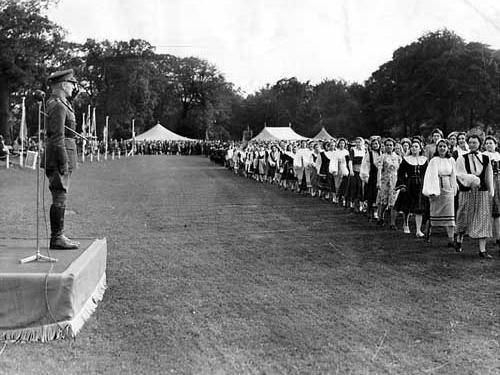 Major General Shiers taking the salute at the march past during Youth Week in September 1942. Demonstrations of dancing were part of the programme, dancers in costume are seen here on the right.