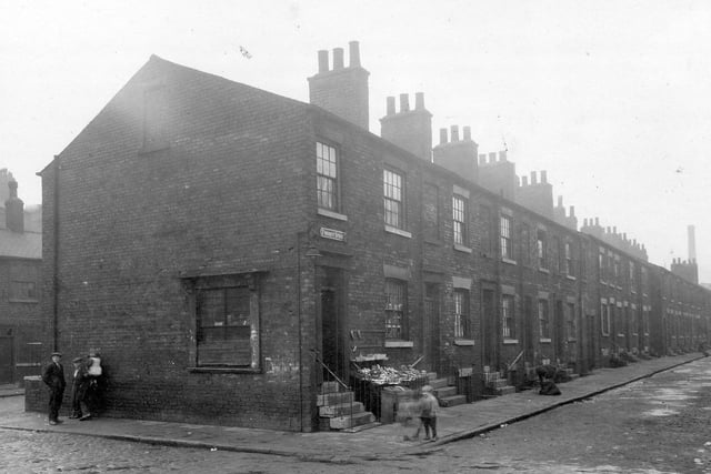 Row of terraced housing on Forrest Street in the West Street area looking west from Wellington Lane. The house on the end of Forrest Street looks to be selling fruit which is piled up on a ledge outside the house.