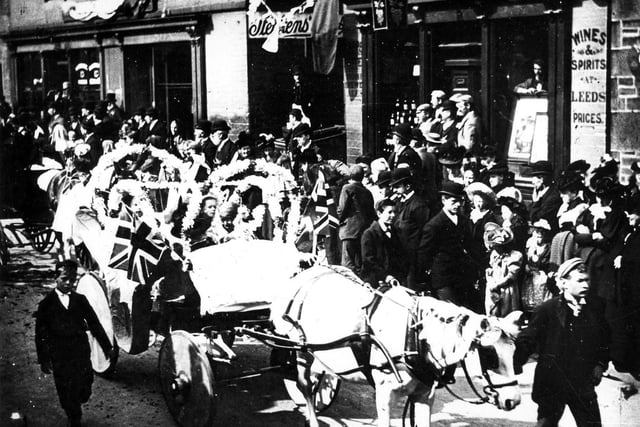 A decorated horse-drawn carriage taking part in the procession at Bramley Carnival, watched by crowds gathered along Town Street. Year unknown.