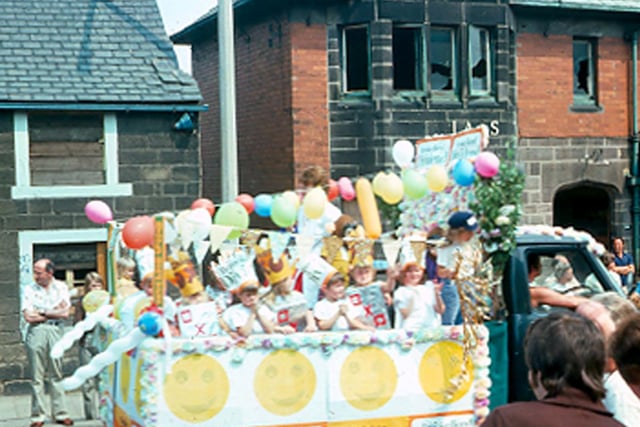 A decorated float parading along Upper Town Street during the Bramley Carnival of July 1976, with people lining the streets to watch.
