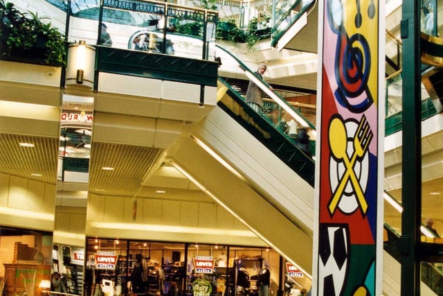 View of three levels of the Centre showing shoppers using escalators. The 'Levi' Jeans shop is visible on the second level.