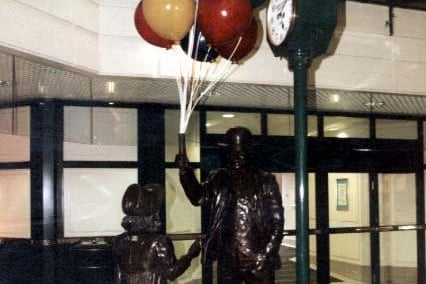 The photograph shows a statue of a man with balloons and a little girl. Next to them is a green and gold clock.