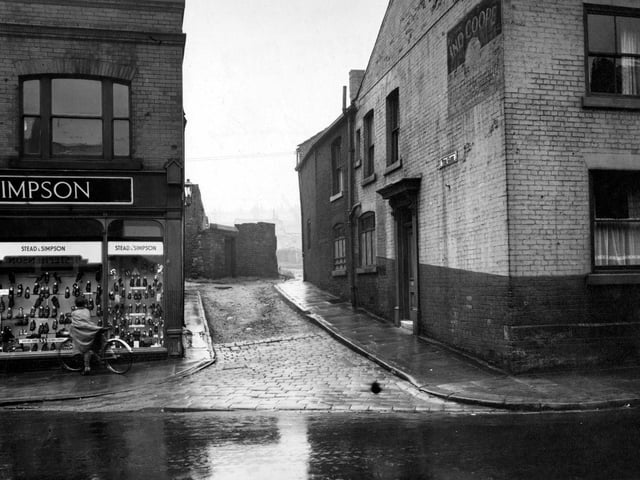 August 1952. View looking south shows The Gang off Town Street. Stead and Simpson shoe shop next door with a man on a bicycle looking in the window.