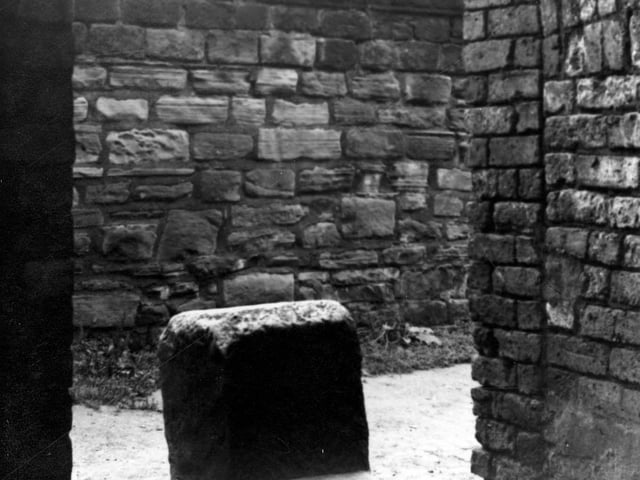 Tower lane in July 1950. View seen from north of mounting blocks, two steps high, next to a brick building near a path with a stone wall with glass on top.