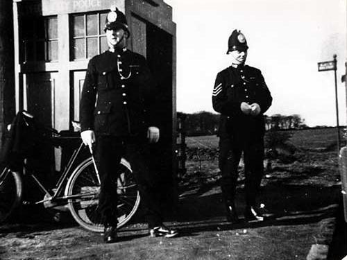 This 1930s image shows two policemen stood by a Leeds City Police Box with a bicycle leaning against the outside. The policeman on the right is a sergeant, this is clear from the three stripes on the arm of his uniform.