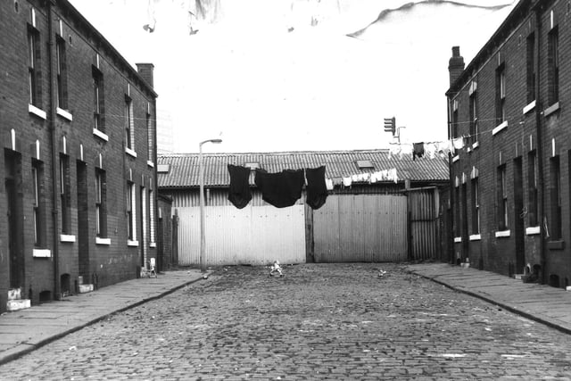 Marion Street in September 1971. On the left are odd numbered houses to the right. Several lines of washing hang across the street. In the centre is part of the premises of Saunders Valve Co Ltd with a corrugated iron wall.