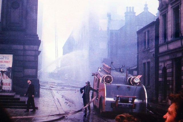 A fire engine and crew at work to extinguish the fire which spread through Morley Town Hall after starting in Albert Mills behind.