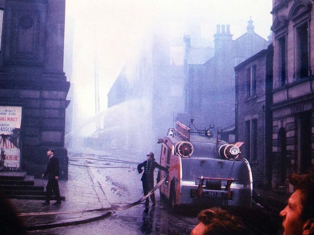 A fire engine and crew at work to extinguish the fire which spread through Morley Town Hall after starting in Albert Mills behind.