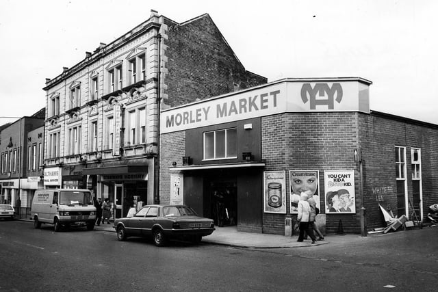 Morley in March 1982. A discount store stands at the junction with Albion Street. Along this parade of shops is Althams travel services, Green's Pork Butchers as well as Stanways Hosiery and an entrance to Morley Market.