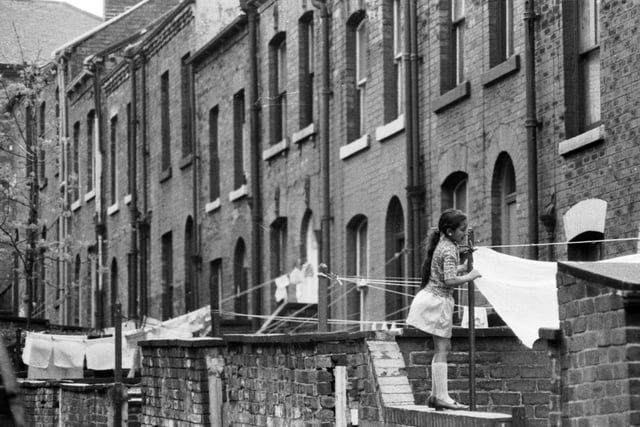 1969. The back of a row of terraced housing which slopes upwards. A young girl is standing on one of the walls to hang out washing. Where in Leeds was this photo taken?