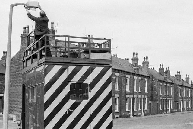 1969. An engineer from the City of Leeds Lighting Department works on a street lamp in the foreground. Rows of terraced housing are in the background but has anyone any idea of the location?