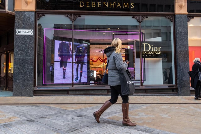 A shopper peers through the window of Debenhams, which is open and trading with a sale