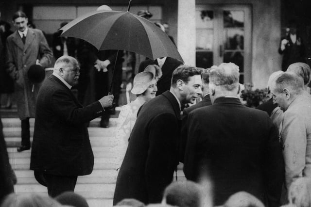 King George VI and Queen Elizabeth their faces alight with interest, chat with ex-servicemen in the rain at The Marine Hall Fleetwood while Lord Derby holds an umbrella over the Queen in 1938