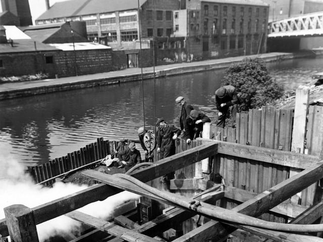 A view shows construction work in progress on a low level sewer on South Accommodation Road by the River Aire. Workmen stand by a crane hook. Airebank Mills and Clarence Glass Works are on the other side of the river. Pictured in May 1950.