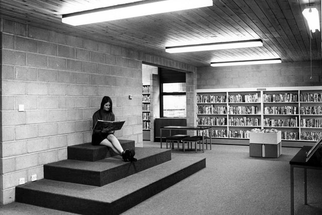 A member of staff poses with a book on a carpeted seating area for children. This arrangement would be suitable for a small audience of young library users at story times.