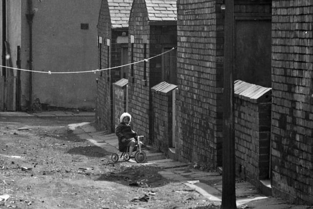A little girl is pictured riding her tricyle along the rear of shops on Tong Road in 1969.