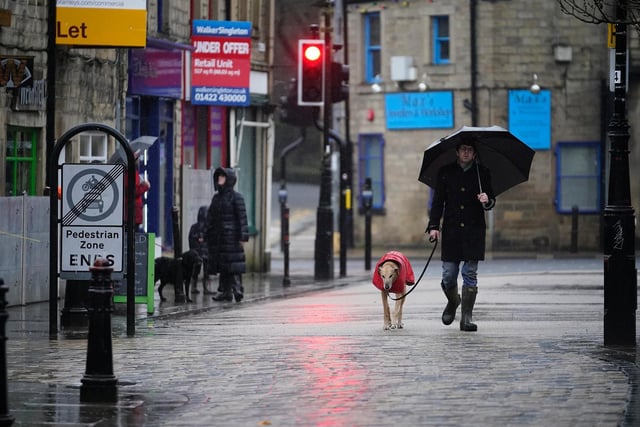 A man and a dog walk in the rain in Hebden Bridge as local shops and businesses install their flood defences