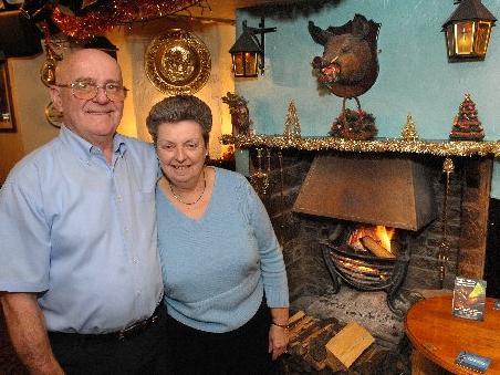 Landlord and landlady Malcolm and Di Meadows, in front of the roaring log fire with a boar's head above it at The Boar's Head, Standish, 2007.