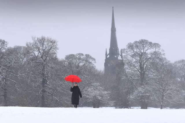A lady walks through the Heavy Snow with Oulton Parish Church, Leeds as a backdrop.