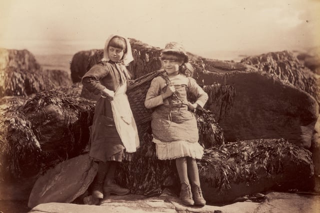 circa 1880: Two young girls stop to rest against a rock.