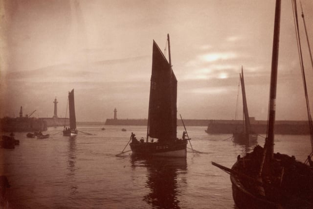 circa 1880: Fishing boats return to Whitby Harbour as the sun goes down.