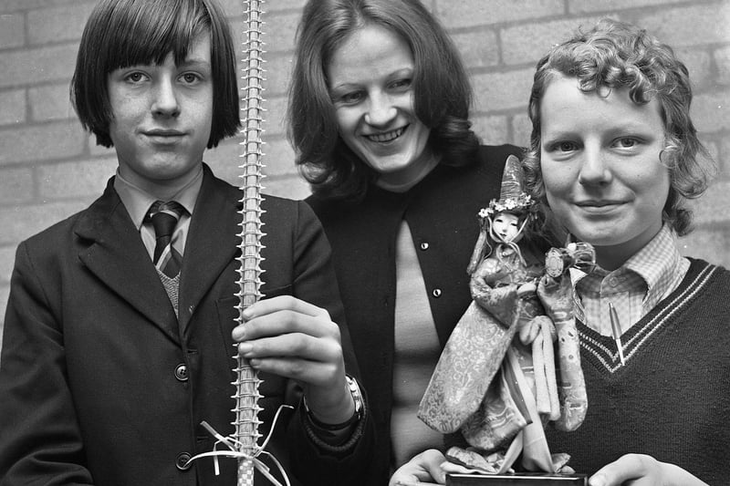 Teacher Miss C.W. Brown with pupils Ian Keegan and Gillian Howarth holding a shark's tooth sword stick from the New Zealand island of Nauru and doll from Taiwan during a Geography lesson in March 1972 at Hindley County Secondary School.