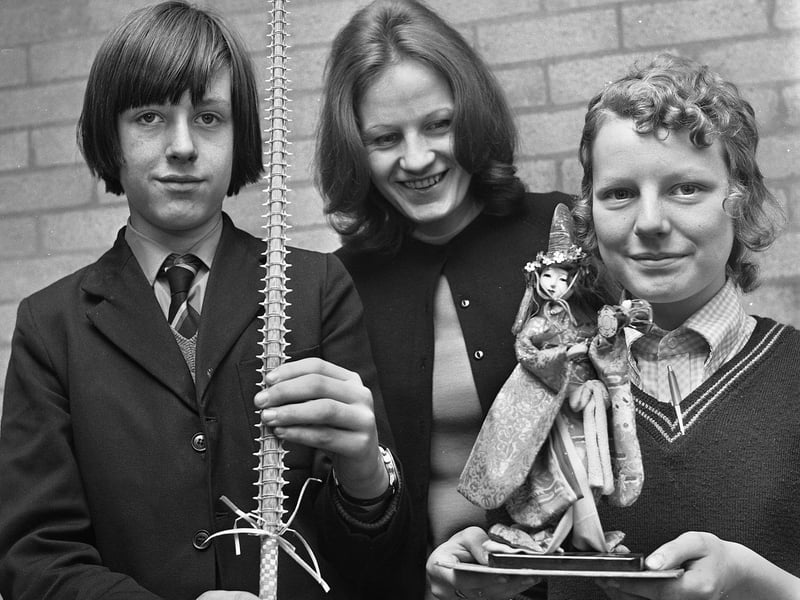Teacher Miss C.W. Brown with pupils Ian Keegan and Gillian Howarth holding a shark's tooth sword stick from the New Zealand island of Nauru and doll from Taiwan during a Geography lesson in March 1972 at Hindley County Secondary School.