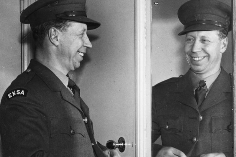 British entertainer George Formby admires in the mirror, dress in his ENSA (Entertainment National Services Association) uniform in 1940.