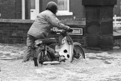 A motorcyclist pushes his bike through the water