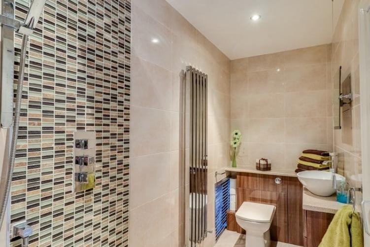 Walk in wet room style shower, downlight spotlights, vanity unit, wash hand basin with mixer tap, low level flush w.c. and central heating radiator, tiling to floor and tiling to walls.