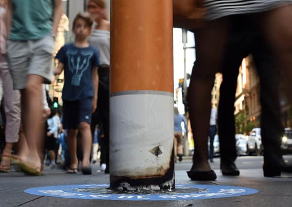 Shoppers walk past a bollard painted to represent a cigarette butt to raise awareness about 'smoke free' zones. Picture: SAEED KHAN/AFP via Getty Images.