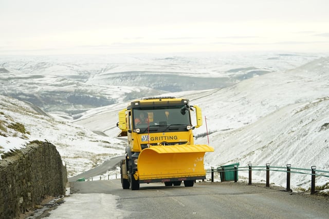 A snow plough and gritting vehicle drives along the snow lined Buttertubs Pass near Hawes in the Yorkshire Dales.