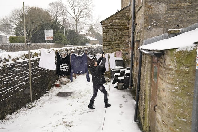 Karen Hesletine stands in a light dusting of snow as she takes in her washing in Hawes, North Yorkshire.