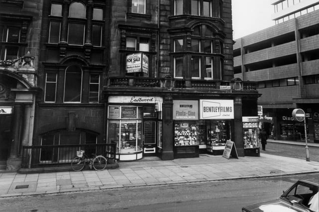 April 1983 and pictured is Albion Place with the YMCA building on the left. Eastwood tobacconists and Bentley Films Ltd. occupy shops on the ground floor. To the right is the junction with Albion Street and the tower block West Riding House, with shops including Dixon's and Curry's at ground level.