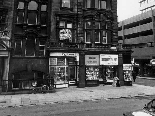 April 1983 and pictured is Albion Place with the YMCA building on the left. Eastwood tobacconists and Bentley Films Ltd. occupy shops on the ground floor. To the right is the junction with Albion Street and the tower block West Riding House, with shops including Dixon's and Curry's at ground level.