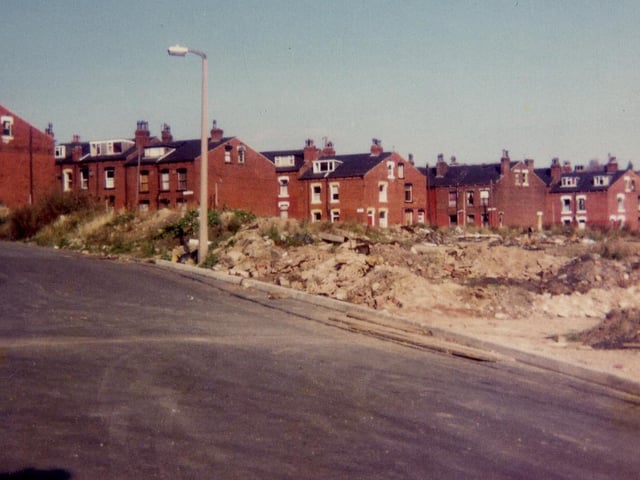 Armley Grove Place pictured in October 1983 showing in the foreground a cleared area where terraced housing has recently been demolished and in the background further rows of housing which are due to be demolished shortly. These are, from left, Fitzarthur Street, Fearnley Street, Gledhow Street and Simpson Street. Middle Cross Street runs across in front of them.