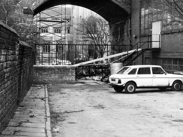 Church Lane, a small lane off New York Street at the side of St. Peter's graveyard which is here blocked off by railings in front of the railway bridge, through which St. Peter's Church, the parish church of Leeds, can be seen in the background.