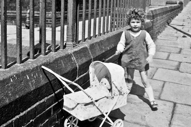 A little girl poses for the camera with her dolls' pram on Claremont Terrace in 1969. Whingate Primary School, which faces on to Whingate Road, dominates the background. This school opened as Whingate Council School in 1886 and remained here until 1989 when a new Whingate Primary School was built on the opposite side of Whingate Road. PIC: Eric Jaquier