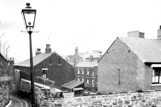 Febriuary 1964 and a gas street lamp lights the entrance to Delph Hill at night, a narrow walkway connecting Seamer Street to Canal Road. The main properties seen are in Pickering Street with part of Carlton Works seen in the background.