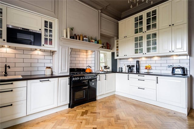The modern fitted kitchen has a range of shaker units with tiled splashbacks and parquet flooring.