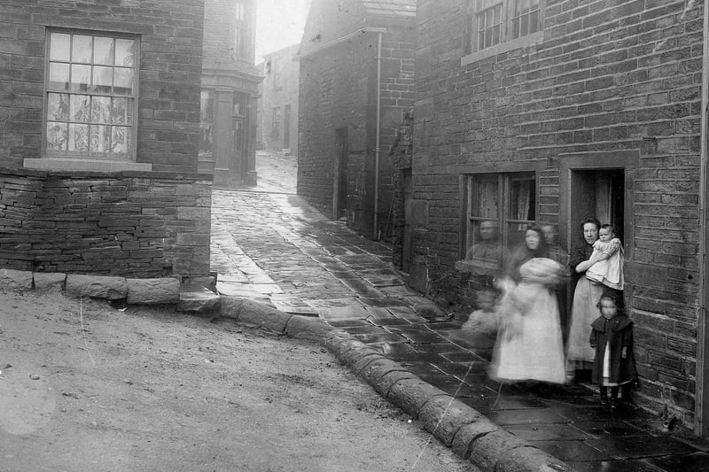 A group of women and children standing in doorway in a back alley or ginnel off Town Street in May 1908.