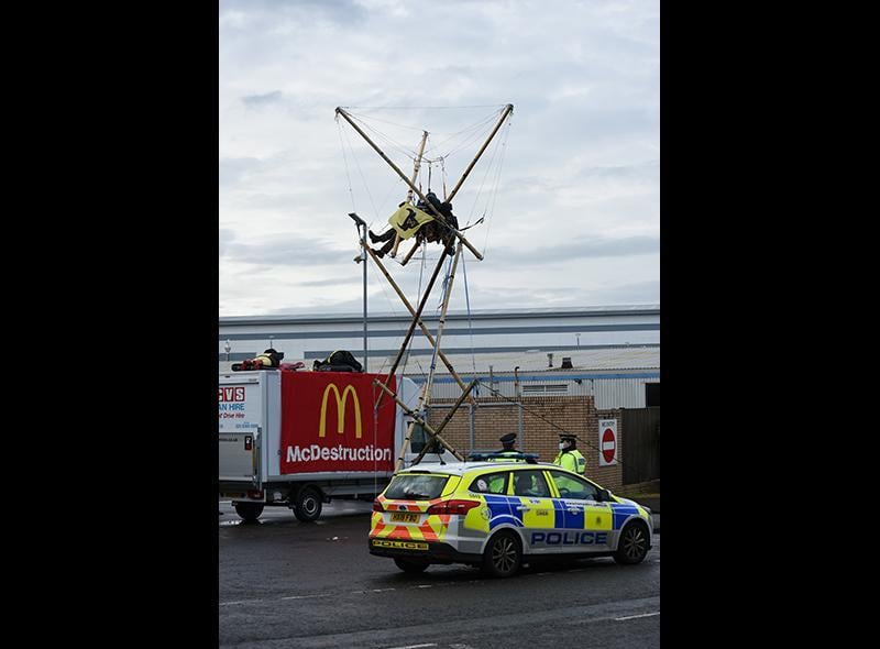 Animal Rebellion protesters suspended from a bamboo structure and on top of a van, being monitored by police officers, outside a McDonalds distribution site in Basingstoke, Hampshire, which is being blockaded to stop lorries from leaving the depot.
