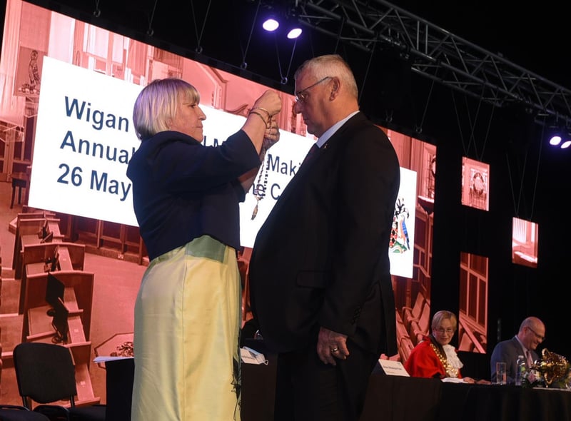 The new deputy mayor Coun Marie Morgan places the chain on consort husband Coun Clive Morgan on stage at the socially distance ceremony at The Edge, Wigan.