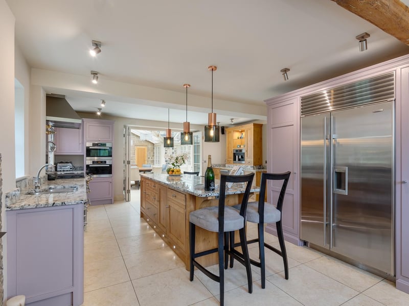 The kitchen boasts integrated appliances such as a wine fridge, as well as a double fridge and a central breakfast island, offering both storage and place to sit and enjoy a meal. The current owners have added a pop of lilac and modern lighting, creating a perfect blend of country-style kitchen and contemporary living.