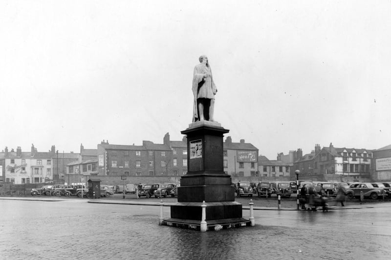 The statue is at the south end of Woodhouse Lane in December 1949. Behind is a car park full of cars.