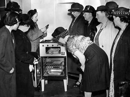 A group of women examine a gas cooker which had four top burners, grill with pan and an oven. It was not unusual for people still to have coal fired ovens and open fires to cook on at this time.