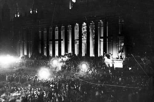 Leeds Town Hall, illuminated by flood lights. Crowds of people can be seen, celebrating VJ Day.