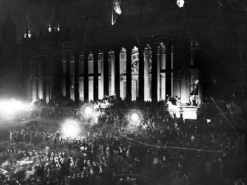 Leeds Town Hall, illuminated by flood lights. Crowds of people can be seen, celebrating VJ Day.